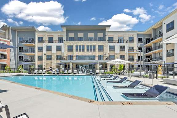 A large swimming pool surrounded by sun loungers in front of apartment buildings at Luxe 360 on Centerpointe Apartments, Virginia