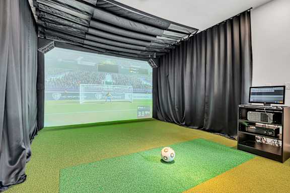 A soccer ball is on a green mat in front of a screen showing a soccer game at Luxe 360 on Centerpointe Apartments, Midlothian, Virginia