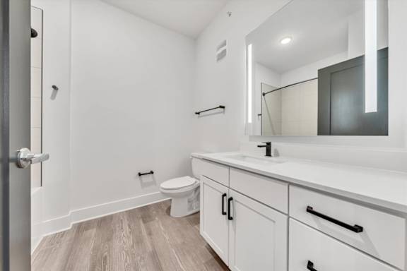 A white bathroom with a toilet, sink, and mirror at Luxe 360 on Centerpointe Apartments, Midlothian, Virginia