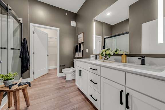 A bathroom with a toilet, sink, and mirror at Luxe 360 on Centerpointe Apartments, Midlothian, VA