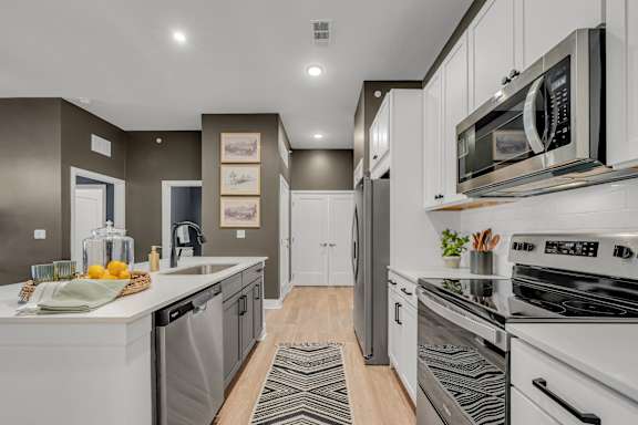 A modern kitchen with white appliances and a wooden floor at Luxe 360 on Centerpointe Apartments, Midlothian, Virginia
