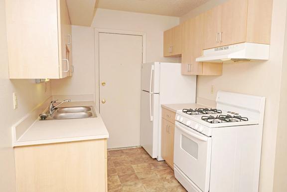 A gallery-style kitchen with a stove, sink, and refrigerator at Madeira Apartments in Kalamazoo, MI