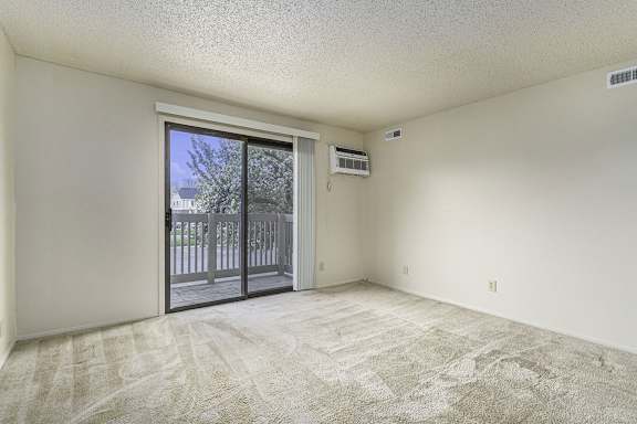 A room with a carpeted floor and a sliding glass door leading to a balcony.