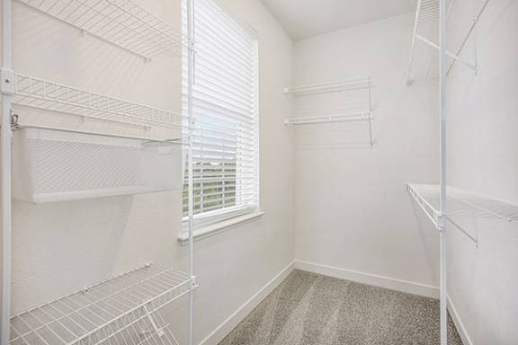 A white walk-in closet with shelves and a window with blinds at Meadowbrooke Apartment Homes in Grand Rapids, MI 49512
