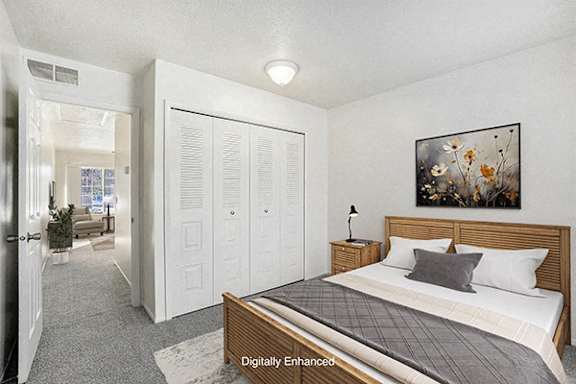A bedroom with a bed, a lamp, and a closet at Newport Village Apartments in Portage, MI 49002