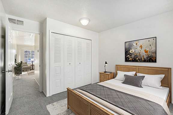 A bedroom with a bed, a lamp, and a closet at Newport Village Apartments in Portage, MI 49002