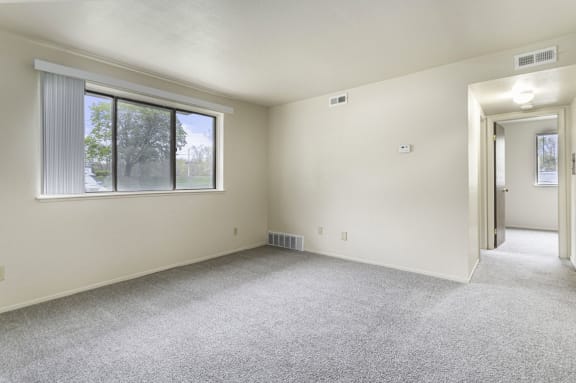 an empty living room with a large window and carpeting a garden style living room with a large window and carpeting at Normandy Village Apartments, Michigan City, IN