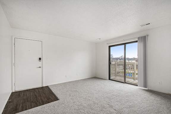 A living room with plush carpet, and a slider to a balcony with a view at Normandy Village Apartments, Michigan City, 46360