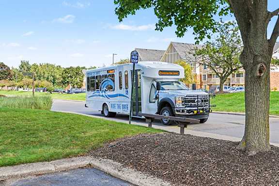 A blue and white bus is stopped at a bus stop with a bench at Normandy Village Apartments in Michigan City, IN