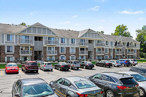 A parking lot with cars and apartment buildings in the background at Normandy Village Apartments in Michigan City, IN