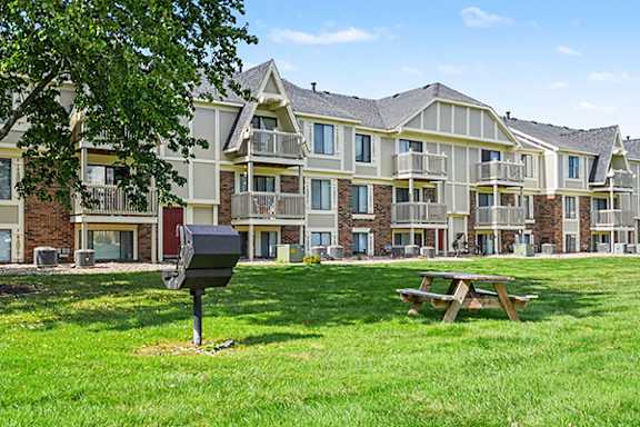 A large building with a grassy area with a picnic table and grill in front at Normandy Village Apartments in Michigan City, IN