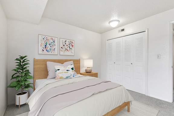 A bedroom with a bed, two pictures on the wall, a potted plant, and a closet door at Old Monterey Apartments, Missouri
