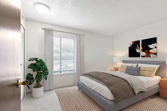 A bedroom with a bed, nightstand, window and a plant at Old Monterey Apartments, Missouri