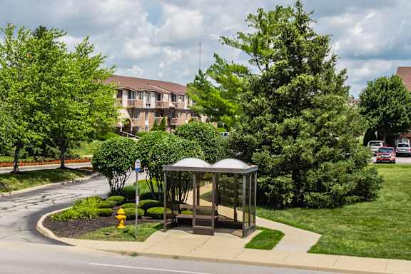 A bus stop with a bench and a yellow fire hydrant in front of a building at Pheasant Run Apartments, Indiana, 47909