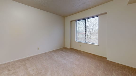 a bedroom with a large window and beige carpeting at Pine Knoll Apartments, Battle Creek, MI