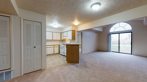 an empty living room with a kitchen and a glass door  at Pine Knoll Apartments, Battle Creek, Michigan