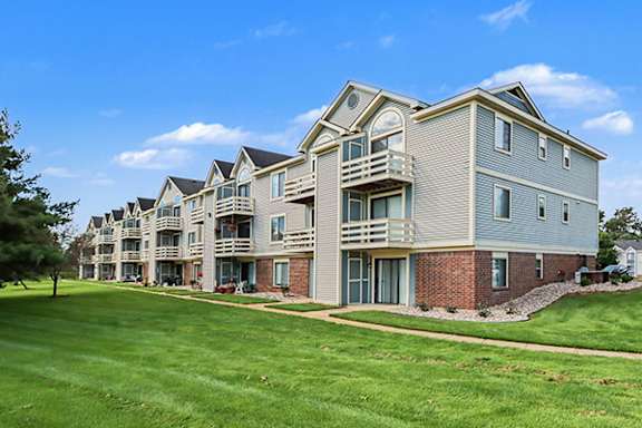 A large apartment building with multiple balconies and a green lawn in front at Pine Knoll Apartments in Battle Creek, MI