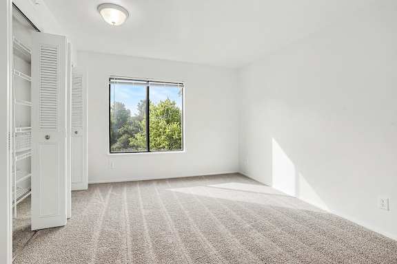 A bedroom with a large window and a carpeted floor at Pine Knoll Apartments, Battle Creek