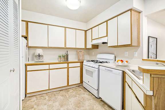 A kitchen with white appliances and wooden cabinets at Pine Knoll Apartments, Battle Creek