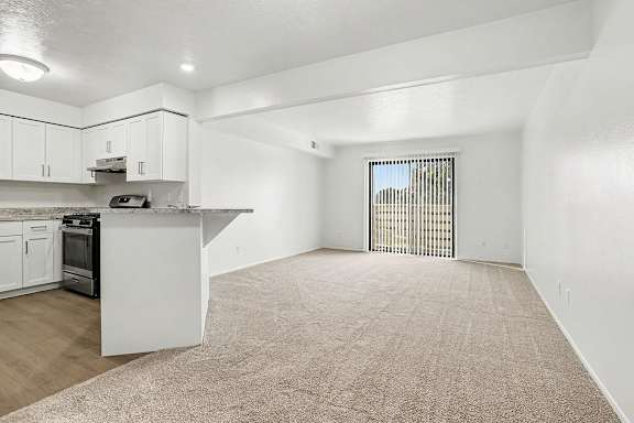 A spacious kitchen with white cabinets and a living room leading to a balcony at Pine Knoll Apartments, Battle Creek