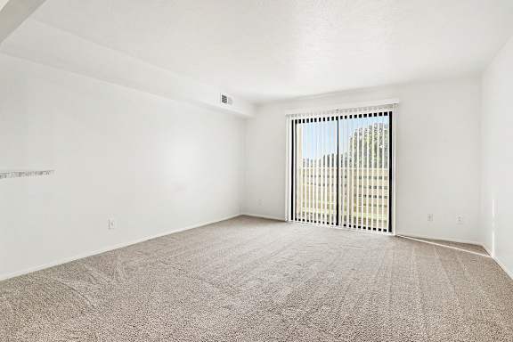 A living room with a carpeted floor and a sliding glass door at Pine Knoll Apartments, Battle Creek