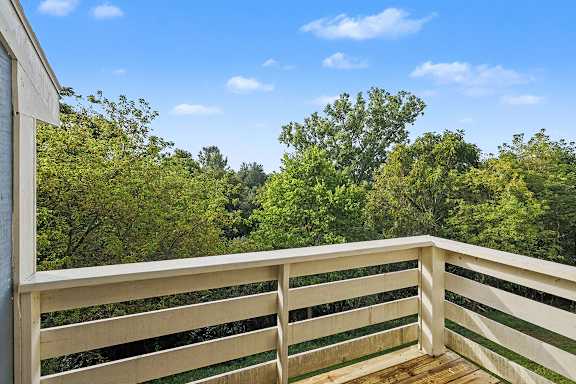 A wooden balcony overlooks a lush green area at Pine Knoll Apartments, Battle Creek
