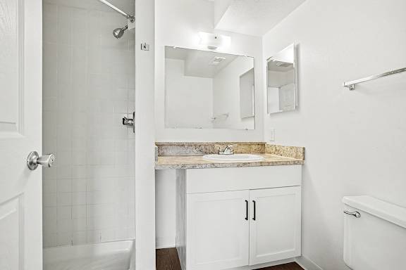 A white bathroom with a shower, sink, and toilet at Pine Knoll Apartments, Battle Creek