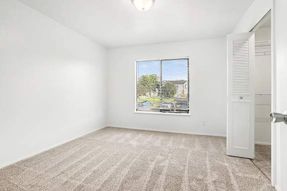 A bedroom with a carpeted floor and a large window at Pine Knoll Apartments, Battle Creek