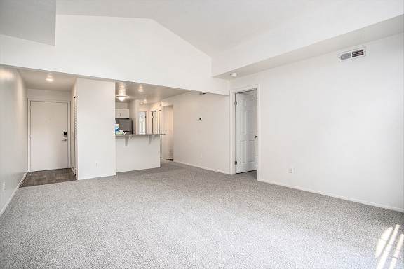 A large, empty living room with a cathedral ceiling and carpeted floor A large, empty living room with a cathedral ceiling and carpeted floor at Pine Knoll Apartments, Battle Creek, 49014
