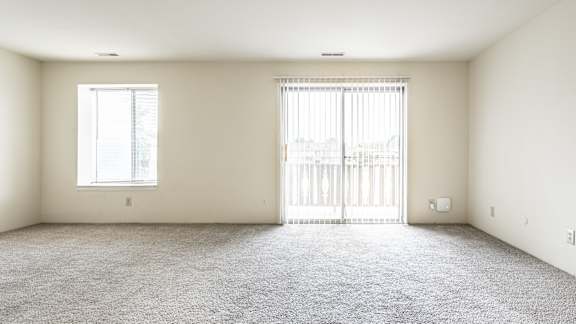 A room with a carpeted floor, a window, and a sliding door.