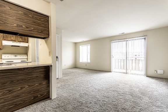 A spacious room with a carpeted floor and a window with blinds.