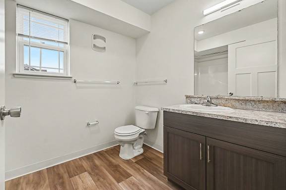 A bathroom with a window, toilet, sink, and hard-surface flooring at The Reserve at The Reserve at Destination Pointe in Grimes, IA 50111