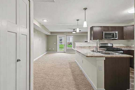 A kitchen with a breakfast bar and a carpeted dining room at The Reserve at The Reserve at Destination Pointe in Grimes, IA 50111