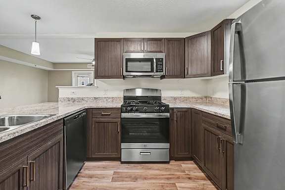 A kitchen with a stainless steel dishwasher and a stove top oven at The Reserve at The Reserve at Destination Pointe in Grimes, IA 50111