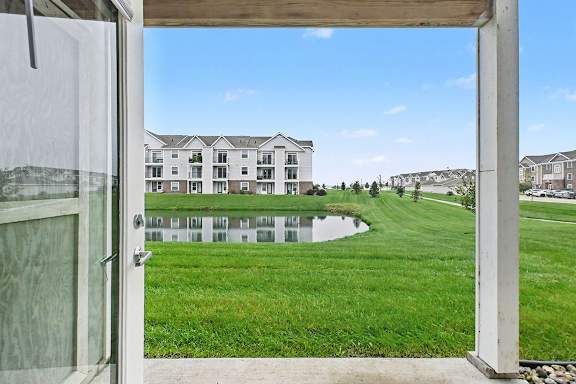 A view of a grassy area from a patio with a building in the background at The Reserve at The Reserve at Destination Pointe in Grimes, IA 50111