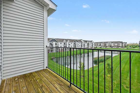 A balcony with a black railing overlooks a grassy area with a large pond at The Reserve at The Reserve at Destination Pointe in Grimes, IA 50111
