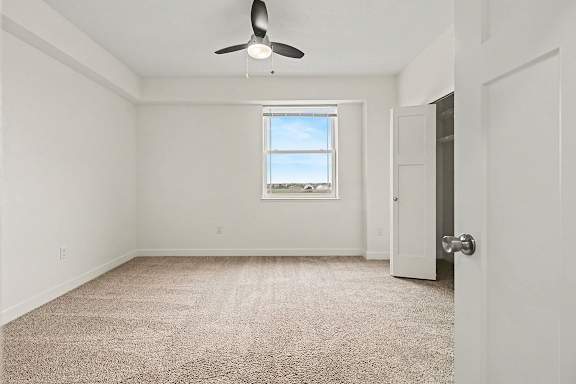 A spacious bedroom with a carpeted floor, a ceiling fan, and a window with a view at The Reserve at The Reserve at Destination Pointe in Grimes, IA 50111
