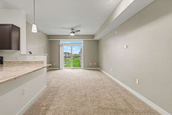 A spacious living and dining room with a carpeted floor and a ceiling fan at The Reserve at The Reserve at Destination Pointe in Grimes, IA 50111