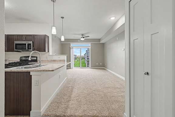 A kitchen with a breakfast bar and a living room with a sliding glass door leading to a balcony at The Reserve at The Reserve at Destination Pointe in Grimes, IA 50111