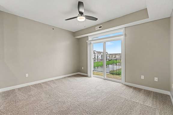A living room with a 9 foot ceiling, ceiling fan and a sliding glass door leading to a balcony at The Reserve at The Reserve at Destination Pointe in Grimes, IA 50111