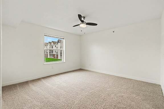 A bedroom with a carpeted floor and a ceiling fan at The Reserve at The Reserve at Destination Pointe in Grimes, IA 50111