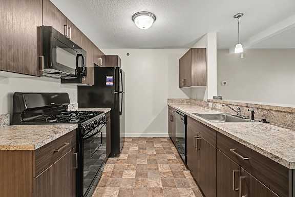 A kitchen with black appliances and brown cabinets at The Reserve at The Reserve at Destination Pointe in Grimes, IA 50111