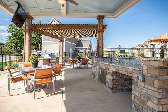 A patio with a stone fireplace and orange chairs. at River Crossing Apartments, St. Charles, MO