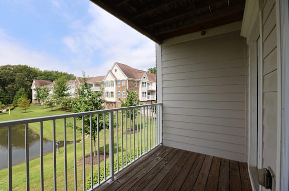 A balcony with a metal railing overlooks a pond and a large building.