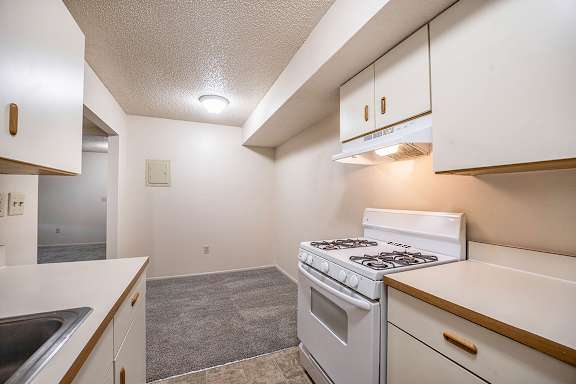 A kitchen with a white stove top oven leading to a dining room at Seville Apartments, Kalamazoo, 49009