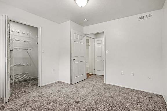A white room with a carpeted floor and a white closet with shelves.