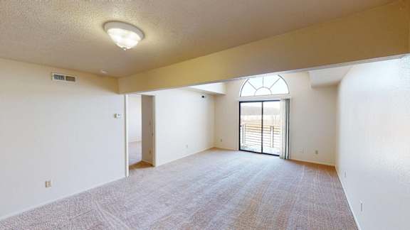 A spacious living room with a carpeted floor and a cathedral ceiling with a large window at South Bridge Apartments, Fort Wayne, Indiana