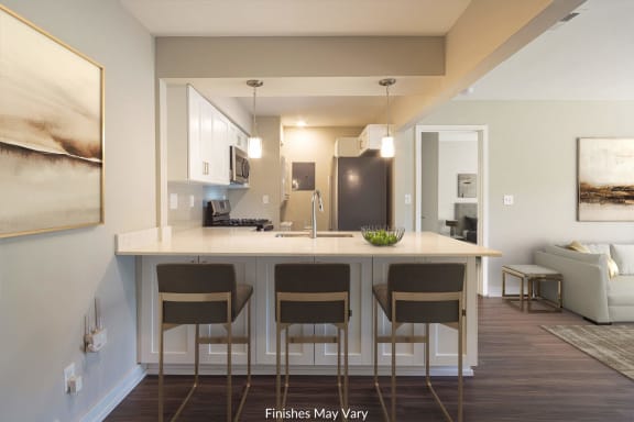 a kitchen with white cabinets and a large island with four stools at Hillside Apartments, Wixom, 48393