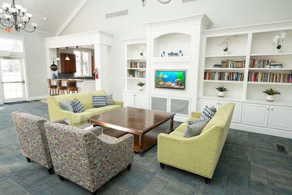 A living room with a yellow couch and a television on a white shelf.