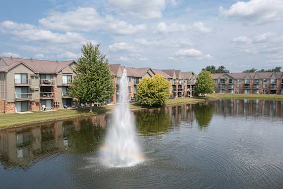 A fountain in the middle of a lake in front of apartment buildings.